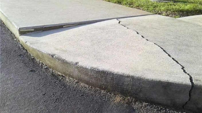 Close-up of a cracked and uneven concrete sidewalk showing signs of neglect and potential safety risk on a commercial property.