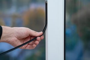 man applying weather stripping to a window seal