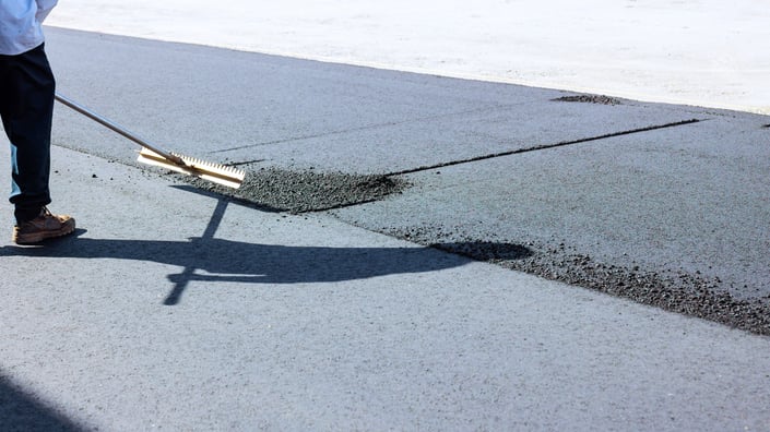 Fresh asphalt being spread across a parking lot surface to repair winter damage and restore pavement conditions during spring maintenance.